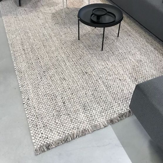 Beige Perletta Doppio vloerkleed in een moderne woonkamer met grijze bank en zwarte salontafel.
