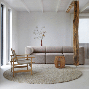 Moderne woonkamer met een Perletta Roundabout vloerkleed, beige bank, houten stoel en decoratieve houten zuil.
