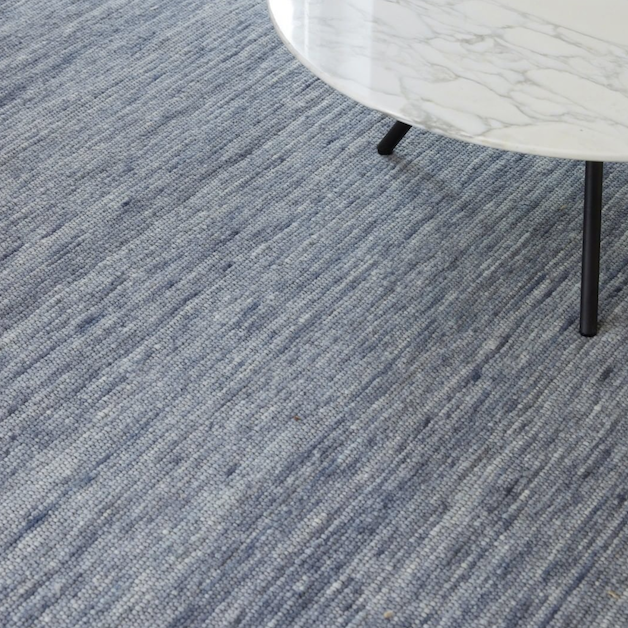 Close-up van een blauw Perletta Spot vloerkleed met een wit marmeren salontafel erop.