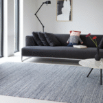 Moderne woonkamer met een grijs Perletta vloerkleed, een donkergrijze bank en een ronde salontafel.