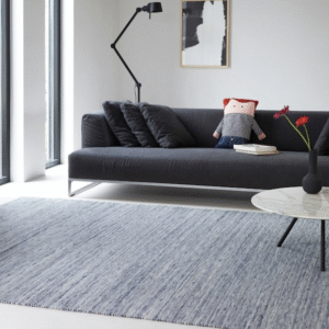 Moderne woonkamer met een grijs Perletta vloerkleed, een donkergrijze bank en een ronde salontafel.