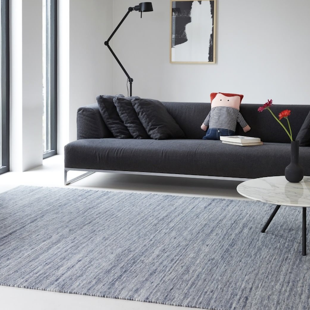 Moderne woonkamer met een grijs Perletta vloerkleed, een donkergrijze bank en een ronde salontafel.