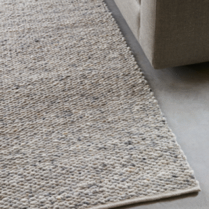 Detailopname van het Perletta Limone vloerkleed naast een beige bank op een betonnen vloer.