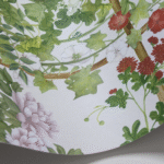 Detail van het Cole and Son Scenic Flora behang met kleurrijke bloemen, groene bladeren en klimplanten op een lichte achtergrond.