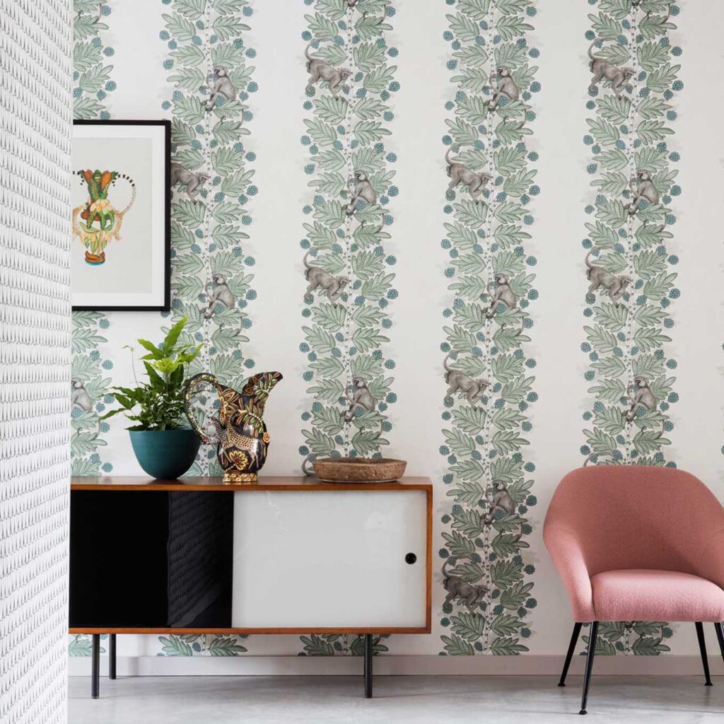 Interieur met Cole and Son Ardmore Acacia 109/11052 behang met groene bladeren en klimmende apen, aangevuld met een roze fauteuil en modern dressoir.
