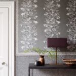 Grijze Ardmore Acacia-behang van Cole and Son met illustraties van apen, bladeren en bessen, gecombineerd met een donkere console en decoratieve objecten.