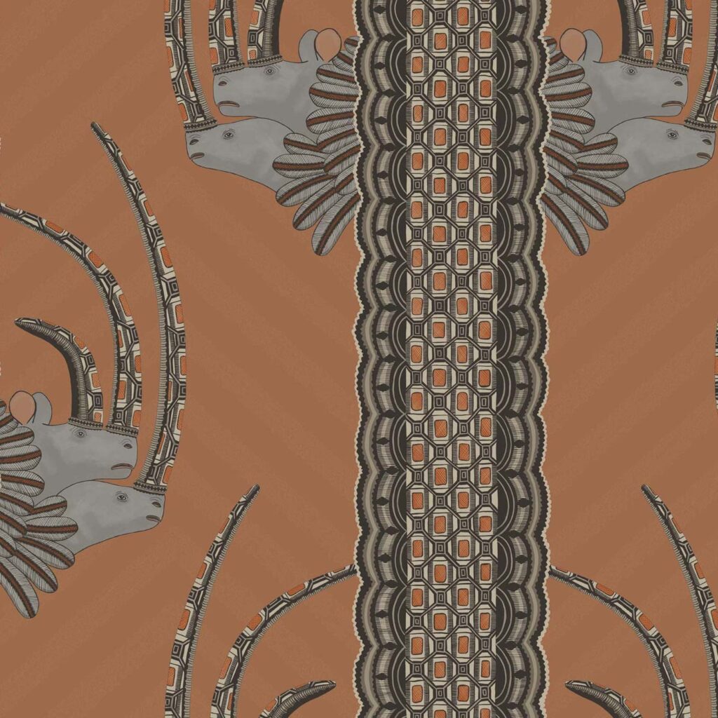 Decoratief patroon uit de Cole & Son Ardmore Jabu collectie met gestileerde antilopekoppen en geometrische motieven op een roestbruine achtergrond.