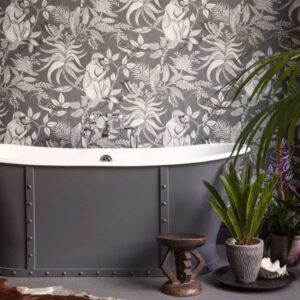 Grijze vrijstaande badkuip voor een wand met Cole and Son Ardmore Savuti behang met apen, vogels en bladeren.