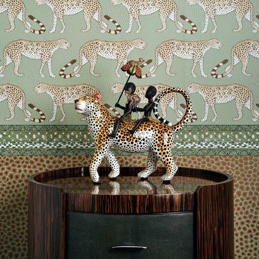 Keramisch beeld van twee figuren op een luipaard, geplaatst op een kastje voor behang met luipaardmotief uit de Cole and Son Ardmore collectie.