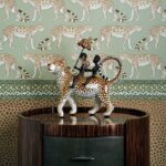 Keramisch beeld van twee figuren op een luipaard, geplaatst op een kastje voor behang met luipaardmotief uit de Cole and Son Ardmore collectie.