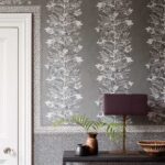 Grijze Ardmore Border-behang van Cole and Son met decoratief patroon van apen in een bladerstructuur, stijlvol gecombineerd met aardewerk en een paarse lamp.