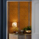 Oranje muur met het Cole and Son Ardmore Border 109/5026 behang, versierd met een gouden kast, lamp en planten.