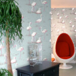 Woonkamer met Cole and Son Flamingos behang, een witte ei-stoel met rood interieur en een zwarte kast.