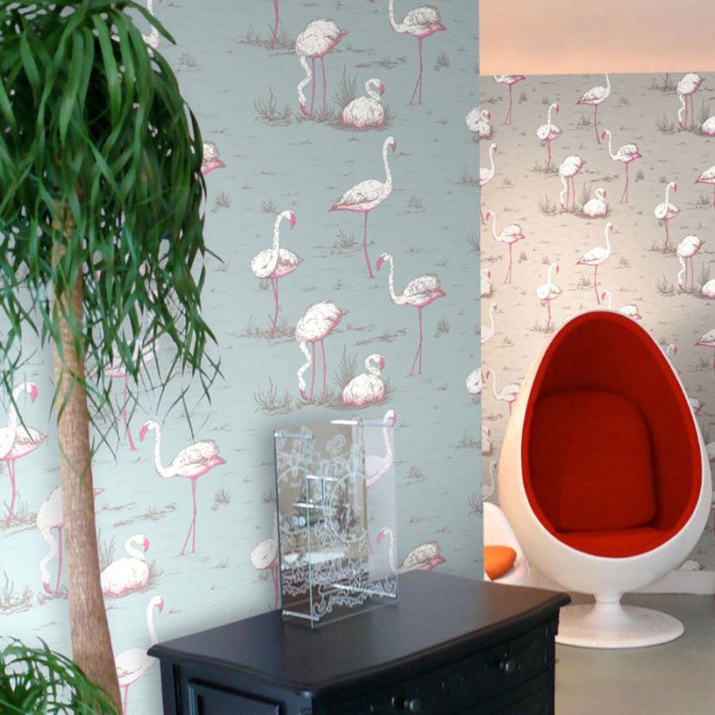 Woonkamer met Cole and Son Flamingos behang, een witte ei-stoel met rood interieur en een zwarte kast.