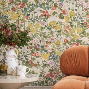 Sfeervolle zithoek met oranje stoel, bloemenbehang van Cole and Son Flora Province en een tafel met bloemenvaas en servies.