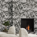 Modern interieur met behang 'Japanese Woods' van Cole and Son, een brandend haardvuur en een bonsaiboom op de voorgrond.