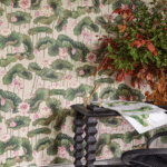 Behang met een patroon van lotusbladeren en -bloemen uit de Cole and Son Lily Lotus collectie, met een zwarte tafel en een vaas met herfstbladeren op de voorgrond.