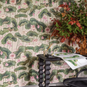 Behang met een patroon van lotusbladeren en -bloemen uit de Cole and Son Lily Lotus collectie, met een zwarte tafel en een vaas met herfstbladeren op de voorgrond.