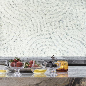 Gedekte marmeren tafel met glazen kommen fruit en kaars, voor een Cole and Son Meditation Stone behang in rustgevend patroon.
