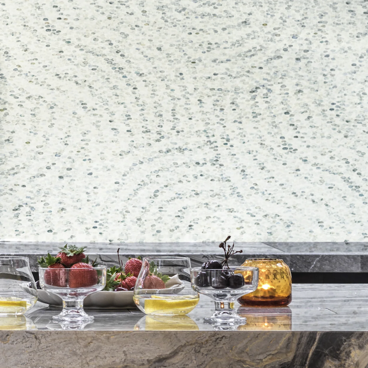 Gedekte marmeren tafel met glazen kommen fruit en kaars, voor een Cole and Son Meditation Stone behang in rustgevend patroon.