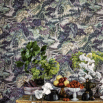 Stilleven met bloemen en fruit op een houten tafel tegen Cole and Son Mountainscape-behang met een schilderachtig berglandschap.