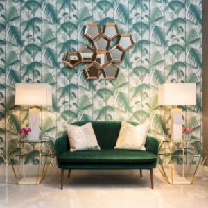 Groene fluwelen bank voor een muur met Cole and Son Palm Jungle behang, omringd door gouden bijzettafels en moderne lampen.