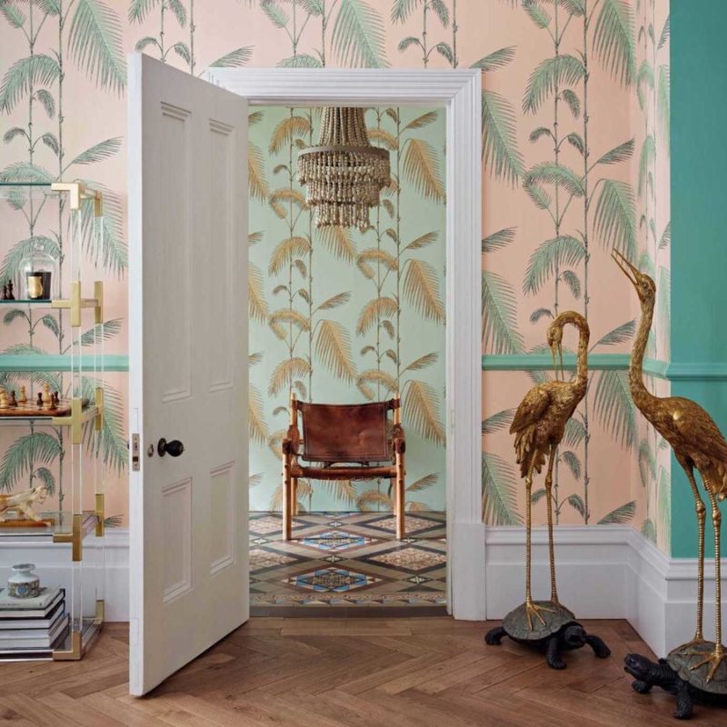Interieur met Cole and Son Palm Leaves Icons-behang, gouden vogelbeelden en een leren stoel in een kleurrijke kamer.
