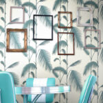 Retro interieur met turquoise stoelen, een metalen tafel en een Cole and Son Palm Leaves behang met lege fotolijsten aan de muur.