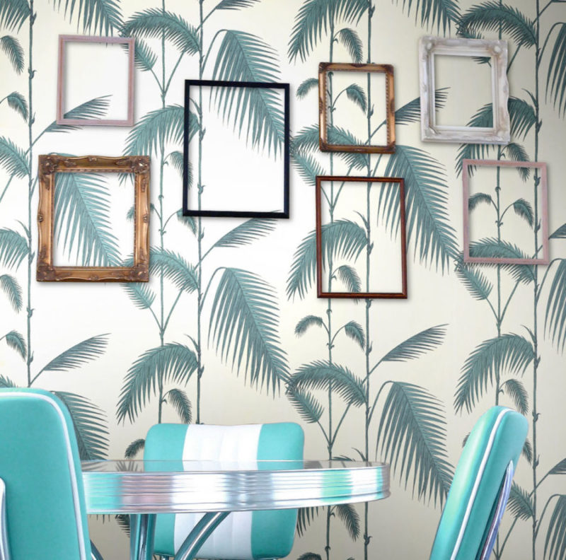 Retro interieur met turquoise stoelen, een metalen tafel en een Cole and Son Palm Leaves behang met lege fotolijsten aan de muur.