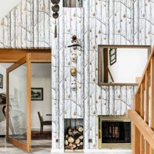 Interieur met Cole and Son Woods and Pears-behang, open haard, houten trapleuning en decoratieve maskers aan de muur.