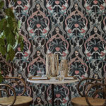 Sfeervolle interieurhoek met een ronde tafel en rotan stoelen tegen het kleurrijke Cole and Son Ardmore Jabula Safari Totem behang.