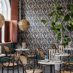 Sfeervolle horecaruimte met het Cole and Son Ardmore Jabula Safari Totem behang, rotanstoelen en grote kamerplant.