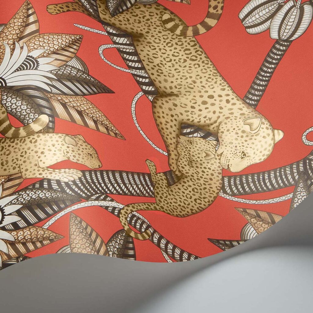 Detail van het Cole and Son Ardmore Jabula behang met luipaarden en gestileerde bladeren op een felrode achtergrond.