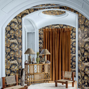 Sfeervolle kamer met Cole and Son Ardmore Jabula 119/3017 Satara behang met dierenmotief, rotanmeubels en goudbruine gordijnen.