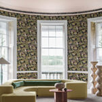 Ronde kamer met grote ramen, modern meubilair en Cole and Son Ardmore Jabula 119/7031 Bush Baby behang met een exotisch patroon.