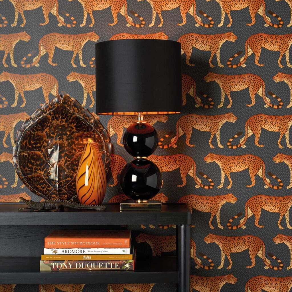 Interieur met Cole and Son Ardmore Leopard Walk behang in oranje en zwart, zwarte lamp en decoratieve accessoires op een zwarte tafel.