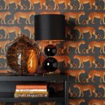 Interieur met Cole and Son Ardmore Leopard Walk behang in oranje en zwart, zwarte lamp en decoratieve accessoires op een zwarte tafel.