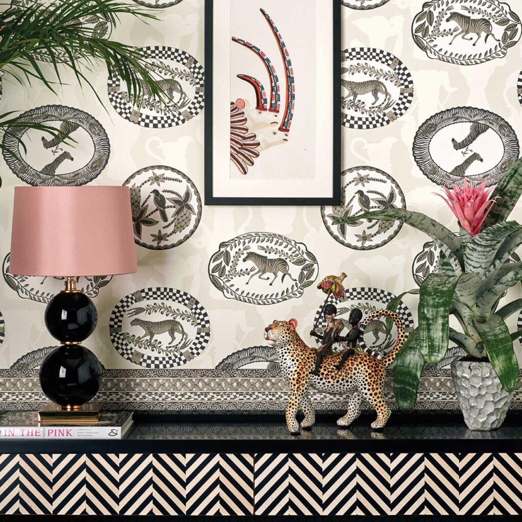 Interieur met Cole and Son-behang Ardmore Matrinah, een zwart-witte dierenprint, gecombineerd met tropische decoraties en een lamp met roze kap.
