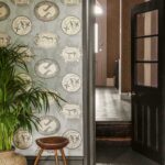Wand met Cole and Son Ardmore Matrinah behang met decoratieve dierenprints in een sfeervol interieur met houten kruk en groene plant.