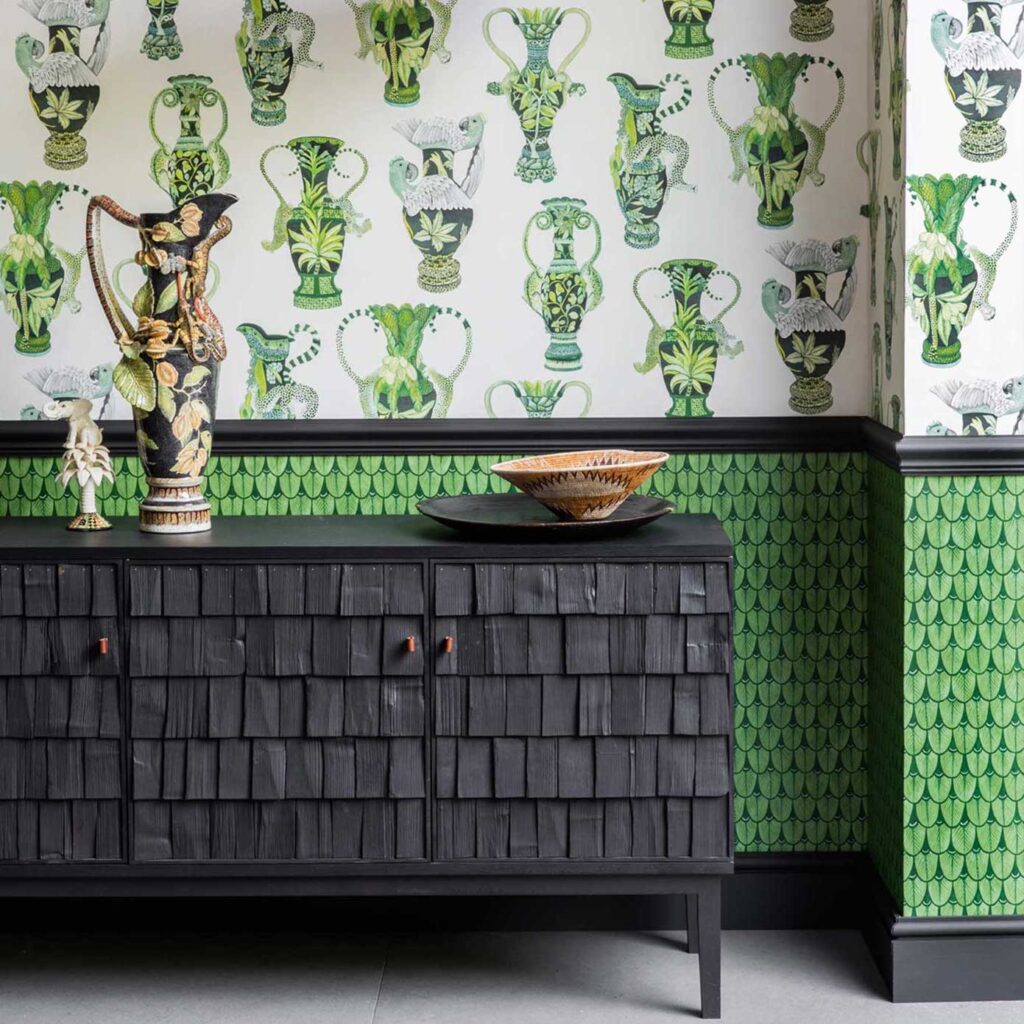 Zwarte houten kast tegen een muur met Cole and Son Ardmore Narina 109/10045 behang met groene exotische vaaspatronen.