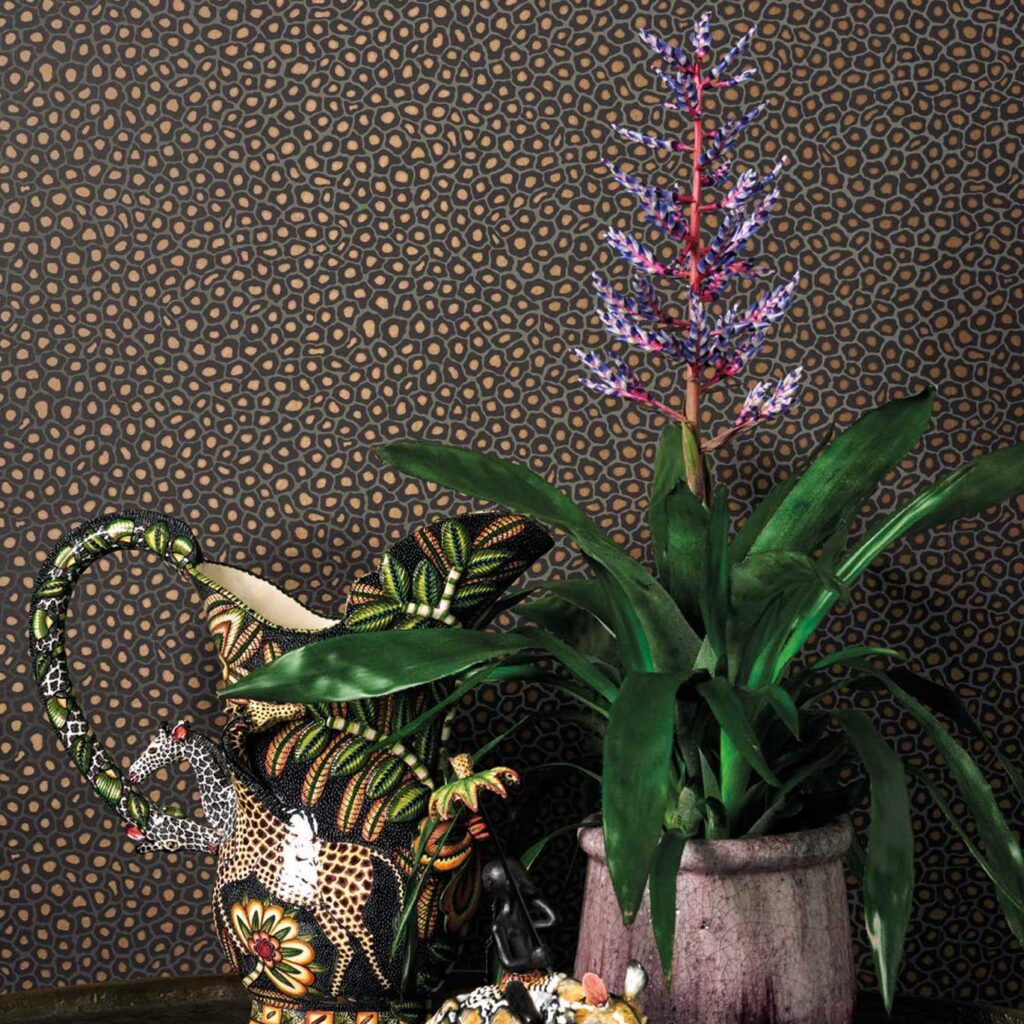 Gekleurd Ardmore Senzo Spot behang van Cole and Son met decoraties en een exotische plant op de voorgrond.