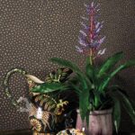 Gekleurd Ardmore Senzo Spot behang van Cole and Son met decoraties en een exotische plant op de voorgrond.