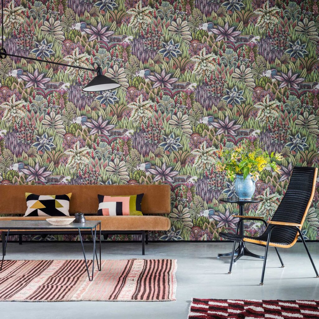 Woonkamer met kleurrijk Ardmore Singita behang van Cole and Son, bruine bank, designstoel en bloemenvaas op bijzettafel.