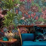 Behang Ardmore Singita van Cole and Son met kleurrijk jungle-patroon, omringd door planten en een fluwelen bank met sierkussen.