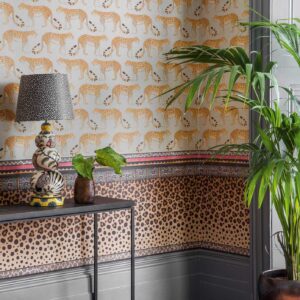 Behang met luipaardpatroon en Afrikaanse motieven uit de Cole and Son Ardmore Zulu Border collectie in een kleurrijk interieur met planten en decoratieve lamp.