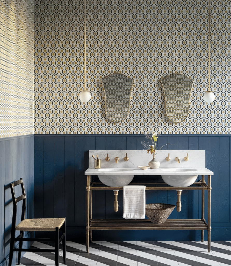 Badkamer met Cole and Son Hicks Hexagon behang, dubbele wastafel met marmeren blad en messing kranen, en blauwe houten lambrisering.