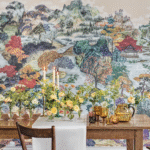Gedekte houten tafel met bloemen en kaarsen voor een kleurrijk Cole & Son Pavilion landschapbehang.
