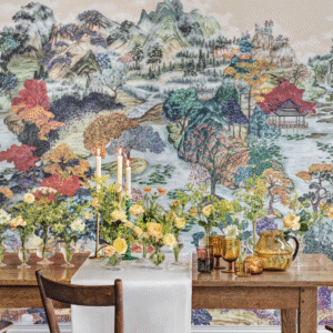 Gedekte houten tafel met bloemen en kaarsen voor een kleurrijk Cole & Son Pavilion landschapbehang.