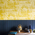 Geel behang met wit Cow Parsley patroon van Cole and Son uit de Contemporary Collection, boven een donkerblauw houten lambrisering en een rustiek houten tafelblad.