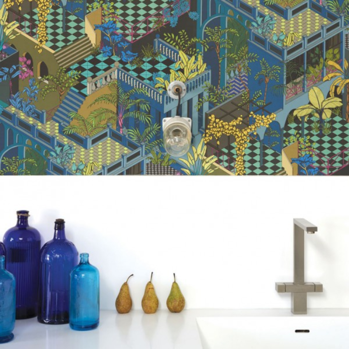 Wand met kleurrijk Cole and Son Miami behang in blauw, gecombineerd met een minimalistisch wit keukenblad met blauwe flessen, peren en een modern kraanarmatuur.